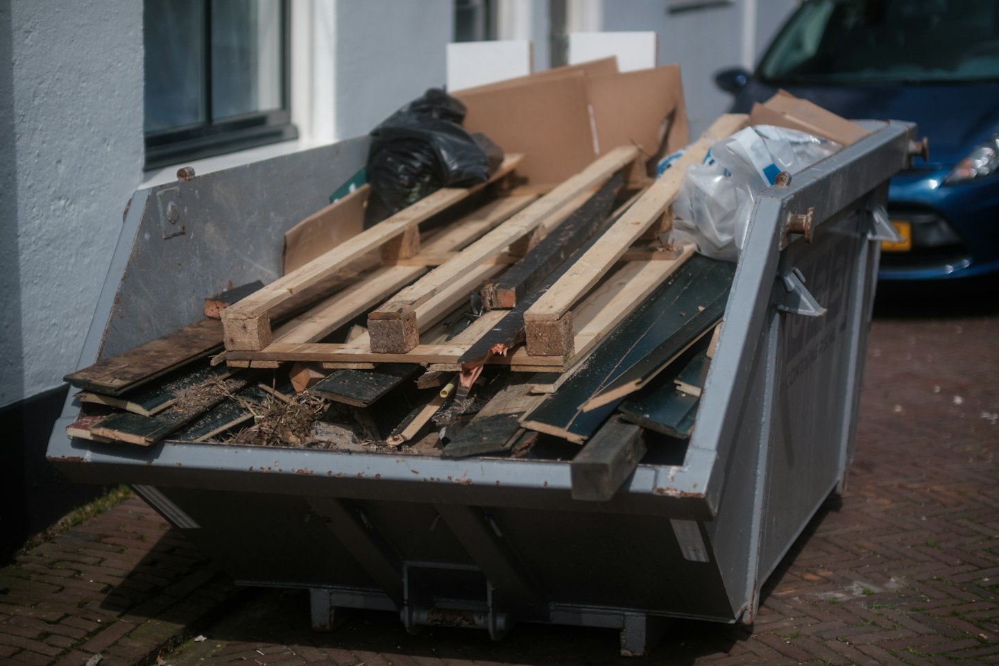 A construction skip bin filled with debris on a paved surface.