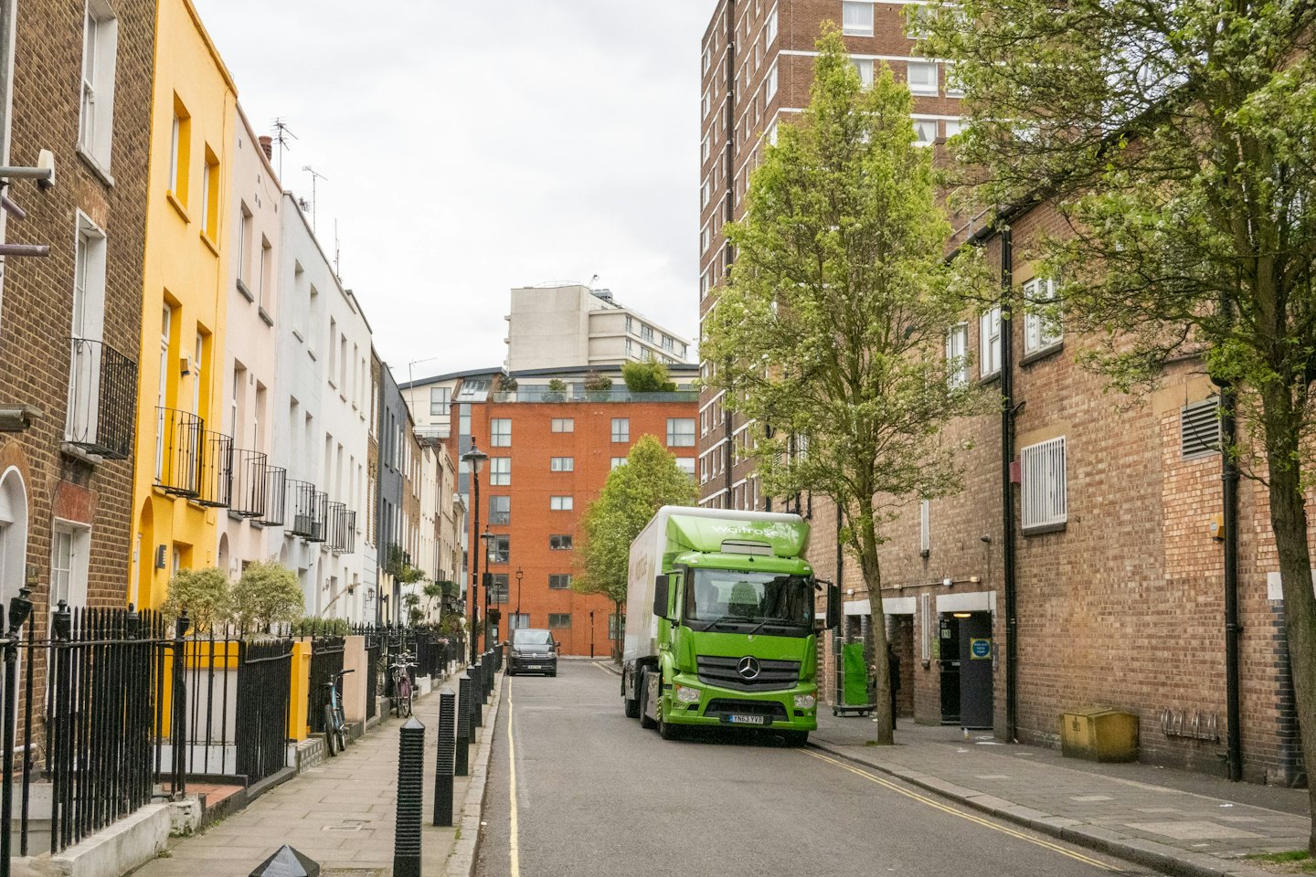 Green delivery truck parked on a narrow city street.