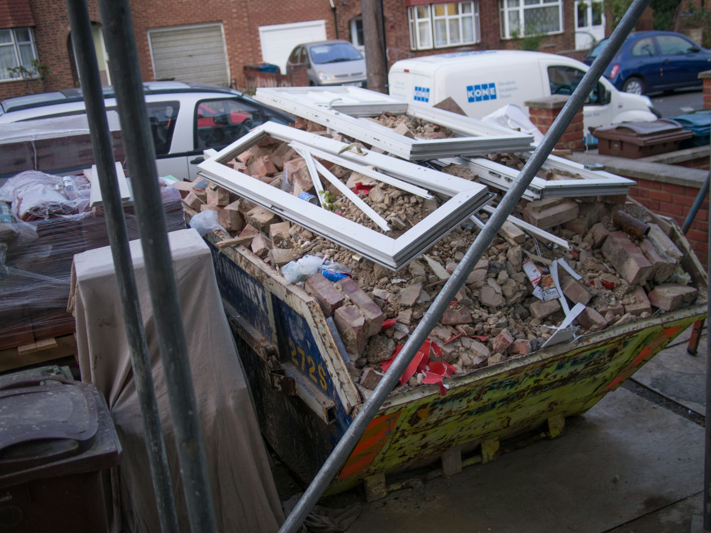 A weathered skip filled with construction rubble sits on a street.
